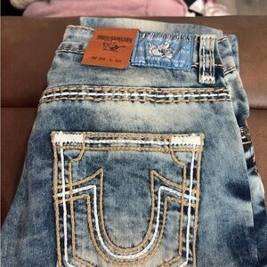 True Religion Blue Jeans with Signature Stitching with rips on each leg.